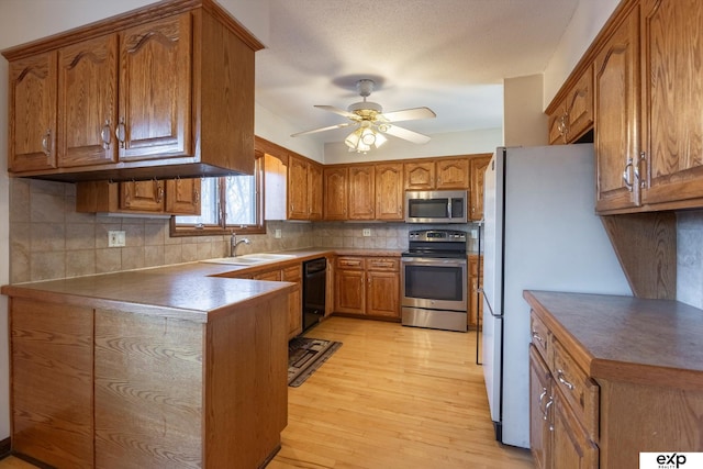 kitchen featuring ceiling fan, appliances with stainless steel finishes, tasteful backsplash, light wood-type flooring, and sink