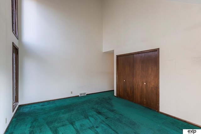 unfurnished bedroom with a closet, a towering ceiling, and dark carpet