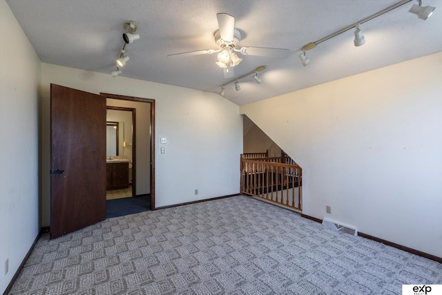 carpeted empty room featuring ceiling fan, rail lighting, a textured ceiling, and lofted ceiling