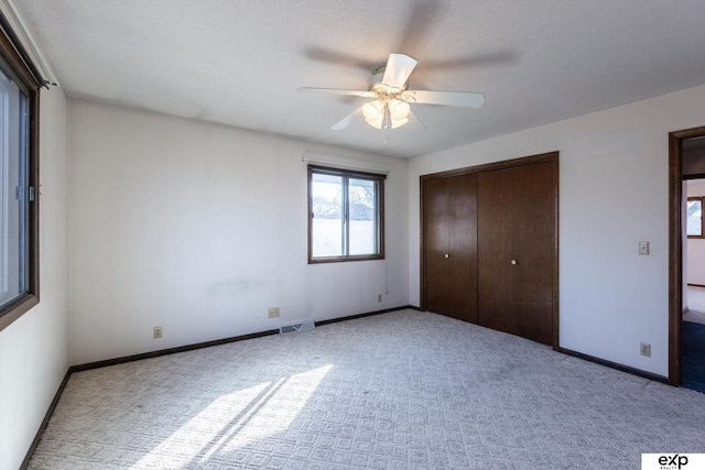 unfurnished bedroom with a textured ceiling, ceiling fan, a closet, and light colored carpet