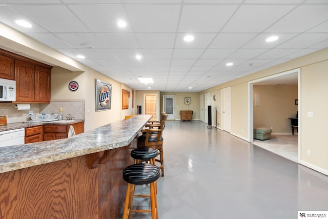 kitchen featuring backsplash, a drop ceiling, sink, white appliances, and a breakfast bar area