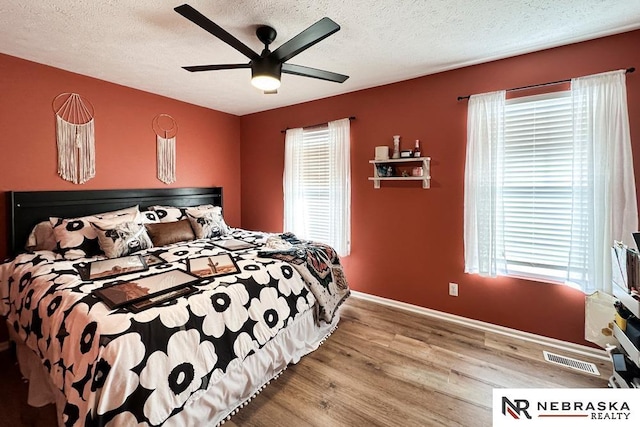 bedroom with a textured ceiling, ceiling fan, wood-type flooring, and multiple windows