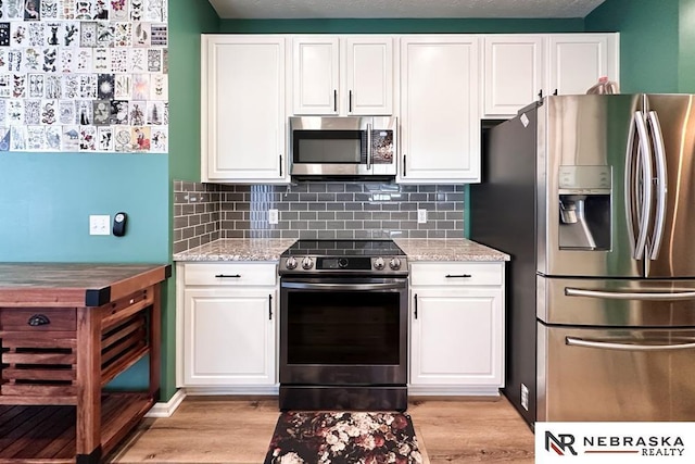 kitchen with white cabinets, light stone counters, and stainless steel appliances