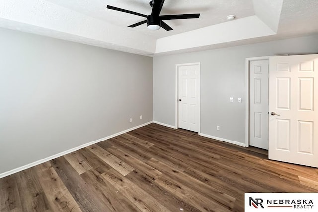 unfurnished bedroom featuring ceiling fan, a textured ceiling, a tray ceiling, and dark hardwood / wood-style floors