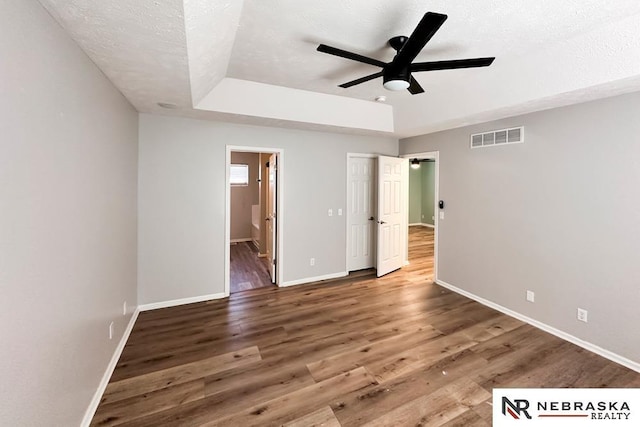 unfurnished bedroom featuring ensuite bath, ceiling fan, a tray ceiling, and a textured ceiling