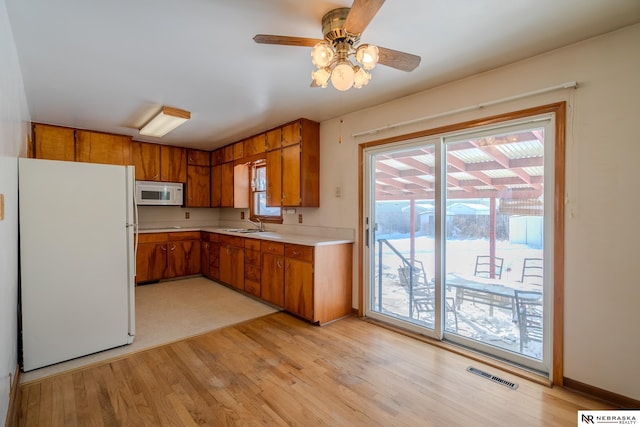 kitchen featuring white appliances, light wood finished floors, visible vents, brown cabinetry, and light countertops