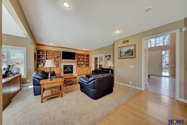 living room with built in shelves, light hardwood / wood-style flooring, and a fireplace