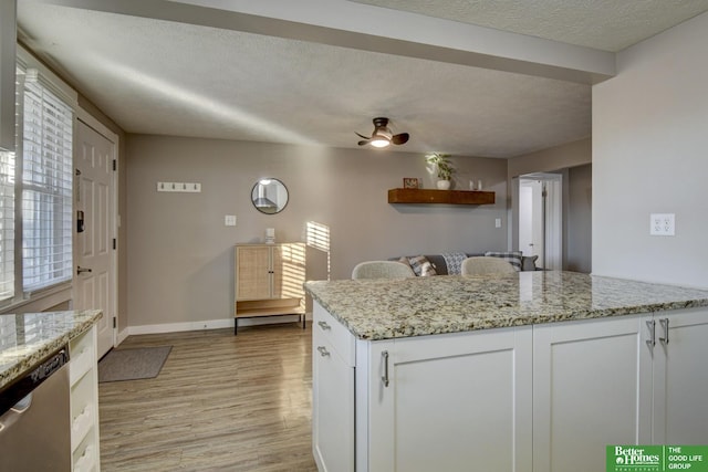 kitchen featuring a textured ceiling, dishwasher, white cabinets, and light stone counters