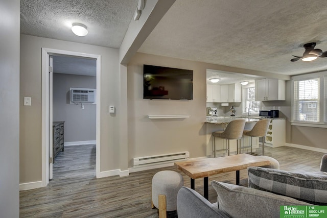 living room featuring hardwood / wood-style floors, a baseboard heating unit, ceiling fan, an AC wall unit, and sink