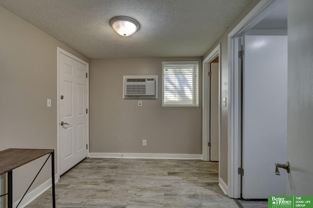 hall with a wall mounted air conditioner, a textured ceiling, and light hardwood / wood-style flooring