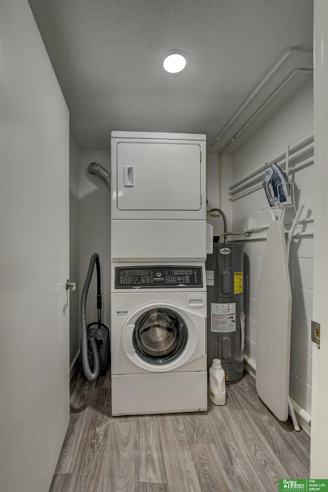 clothes washing area with a textured ceiling, stacked washer and clothes dryer, water heater, and light wood-type flooring