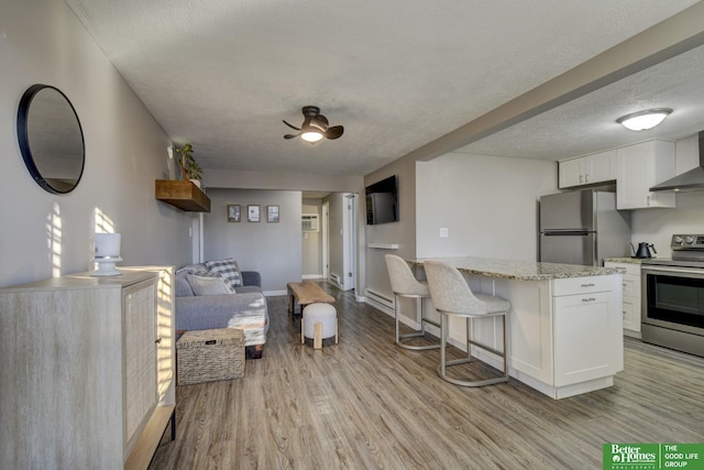 kitchen with white cabinetry, a breakfast bar area, stainless steel appliances, a textured ceiling, and light hardwood / wood-style flooring