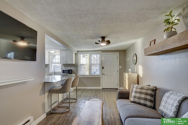 living room with light hardwood / wood-style floors, a textured ceiling, a baseboard heating unit, and ceiling fan