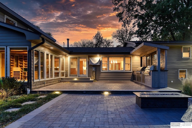 back house at dusk featuring exterior kitchen, a fire pit, and a patio