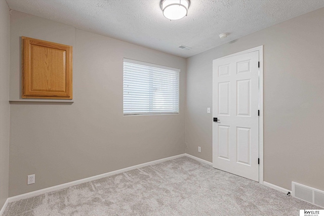 spare room with light colored carpet and a textured ceiling