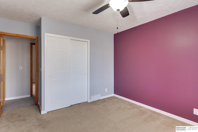 unfurnished bedroom with ceiling fan, light colored carpet, a textured ceiling, and a closet