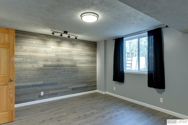 empty room with hardwood / wood-style flooring, wooden walls, a textured ceiling, and rail lighting