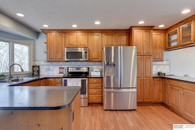 kitchen with backsplash, appliances with stainless steel finishes, sink, and light hardwood / wood-style flooring