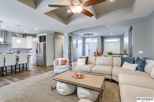 living room featuring light wood-type flooring, ceiling fan, a tray ceiling, and sink