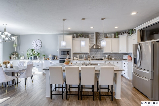 kitchen featuring white cabinets, hanging light fixtures, appliances with stainless steel finishes, and an island with sink