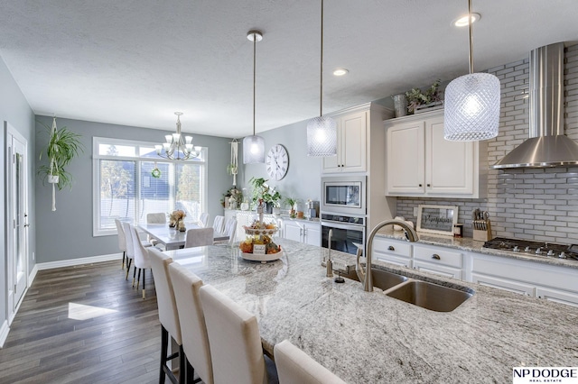 kitchen with white cabinetry, stainless steel appliances, sink, hanging light fixtures, and light stone counters