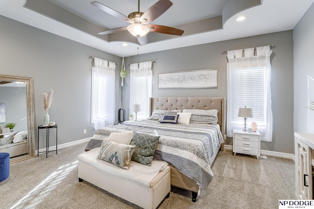 bedroom featuring ceiling fan, light colored carpet, and a tray ceiling