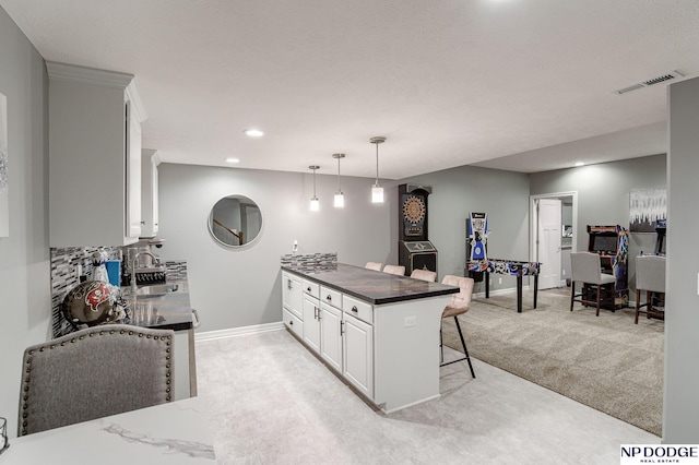 kitchen with decorative light fixtures, backsplash, a kitchen bar, light carpet, and white cabinets