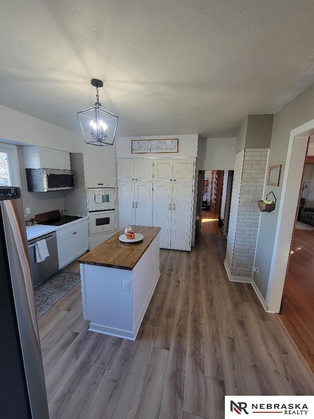 kitchen featuring wood counters, stainless steel appliances, decorative light fixtures, a kitchen island, and white cabinets