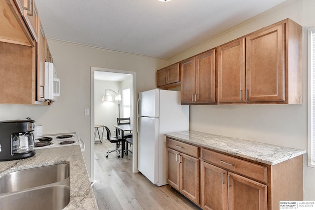 kitchen featuring light stone countertops, sink, light hardwood / wood-style flooring, and white appliances