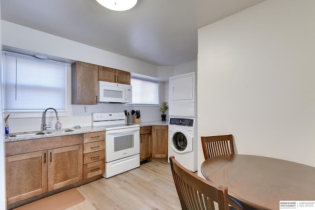 kitchen featuring light hardwood / wood-style floors, white appliances, stacked washer / dryer, light stone countertops, and sink