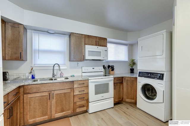 kitchen featuring white appliances, sink, stacked washing maching and dryer, light wood-type flooring, and light stone counters