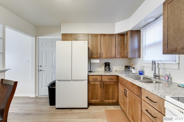 kitchen with electric range oven, white fridge, sink, light hardwood / wood-style flooring, and light stone countertops