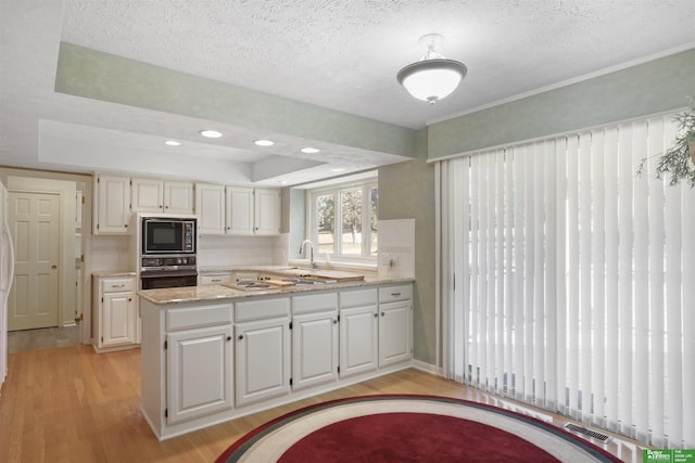 kitchen with white cabinets, black microwave, kitchen peninsula, oven, and a raised ceiling