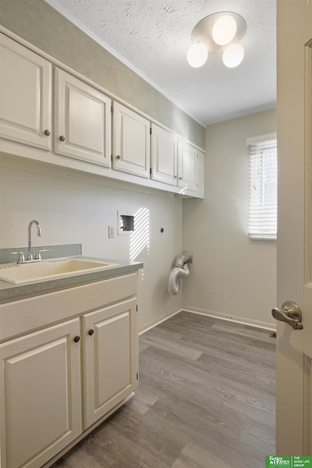 laundry room featuring electric dryer hookup, wood-type flooring, a textured ceiling, cabinets, and sink