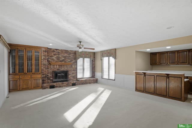 unfurnished living room featuring ceiling fan, light colored carpet, a textured ceiling, and a fireplace