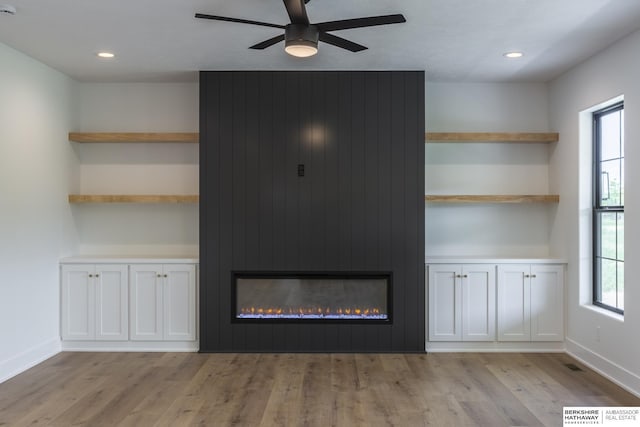 unfurnished living room featuring light wood-type flooring, ceiling fan, built in features, and a fireplace