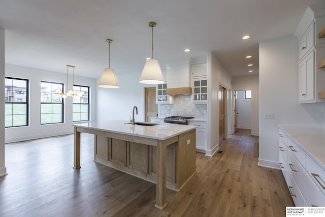 kitchen with premium range hood, white cabinetry, a center island with sink, backsplash, and sink