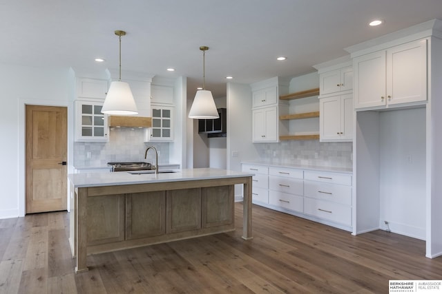 kitchen with sink, hanging light fixtures, white cabinets, and a center island with sink