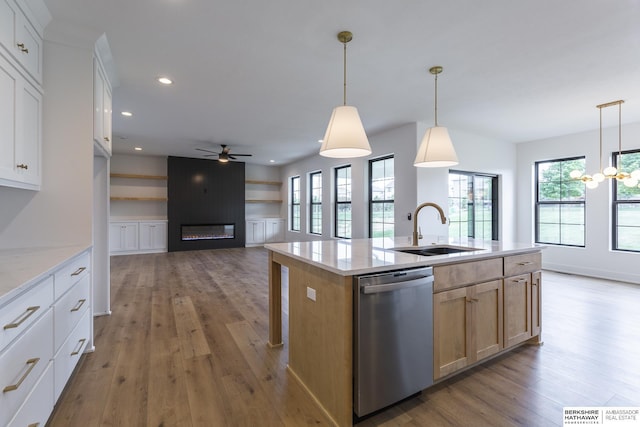 kitchen featuring white cabinetry, an island with sink, decorative light fixtures, a large fireplace, and stainless steel dishwasher