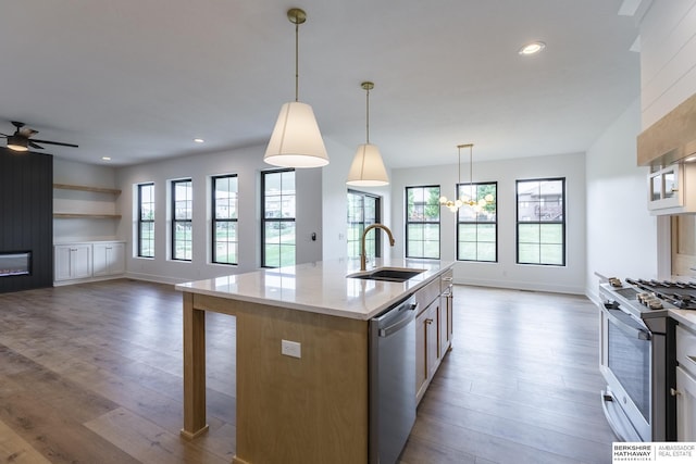 kitchen with appliances with stainless steel finishes, a kitchen island with sink, decorative light fixtures, ceiling fan with notable chandelier, and sink