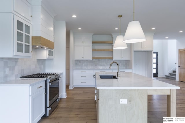 kitchen featuring an island with sink, stainless steel gas range, hanging light fixtures, white cabinets, and sink