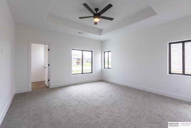 empty room with ceiling fan, light colored carpet, and a tray ceiling