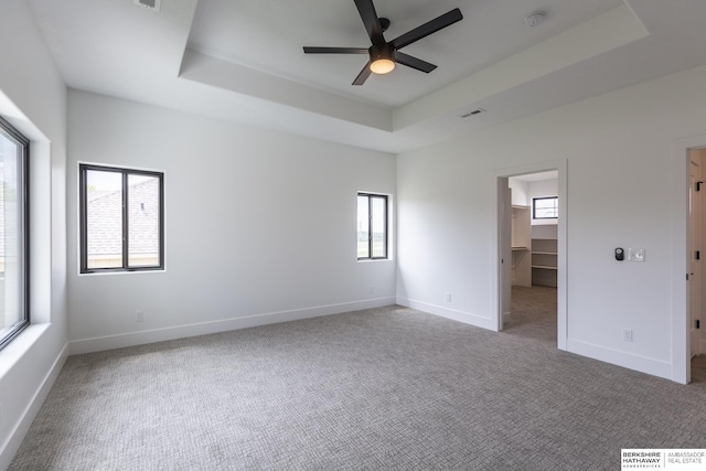 unfurnished bedroom with ceiling fan, a walk in closet, a tray ceiling, and multiple windows