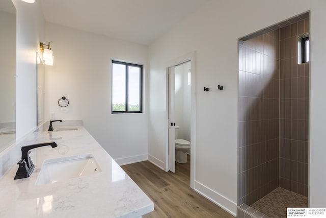 bathroom with toilet, vanity, wood-type flooring, and tiled shower