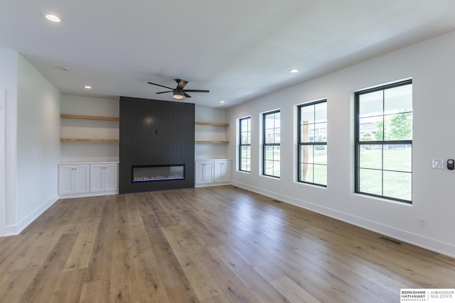 unfurnished living room with ceiling fan, light wood-type flooring, and a large fireplace