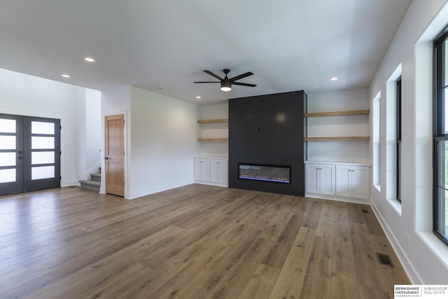 unfurnished living room featuring ceiling fan, a large fireplace, french doors, and light wood-type flooring