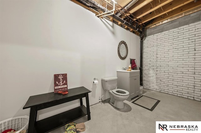 bathroom with toilet, brick wall, concrete floors, and vanity