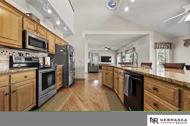 kitchen with ceiling fan, vaulted ceiling, decorative backsplash, appliances with stainless steel finishes, and light stone counters