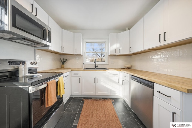 kitchen featuring white cabinetry, wooden counters, stainless steel appliances, dark tile patterned flooring, and sink