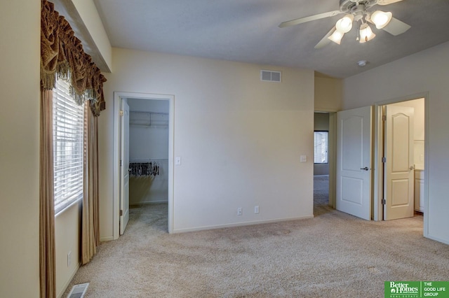 unfurnished bedroom with light carpet, ceiling fan, a walk in closet, and a closet